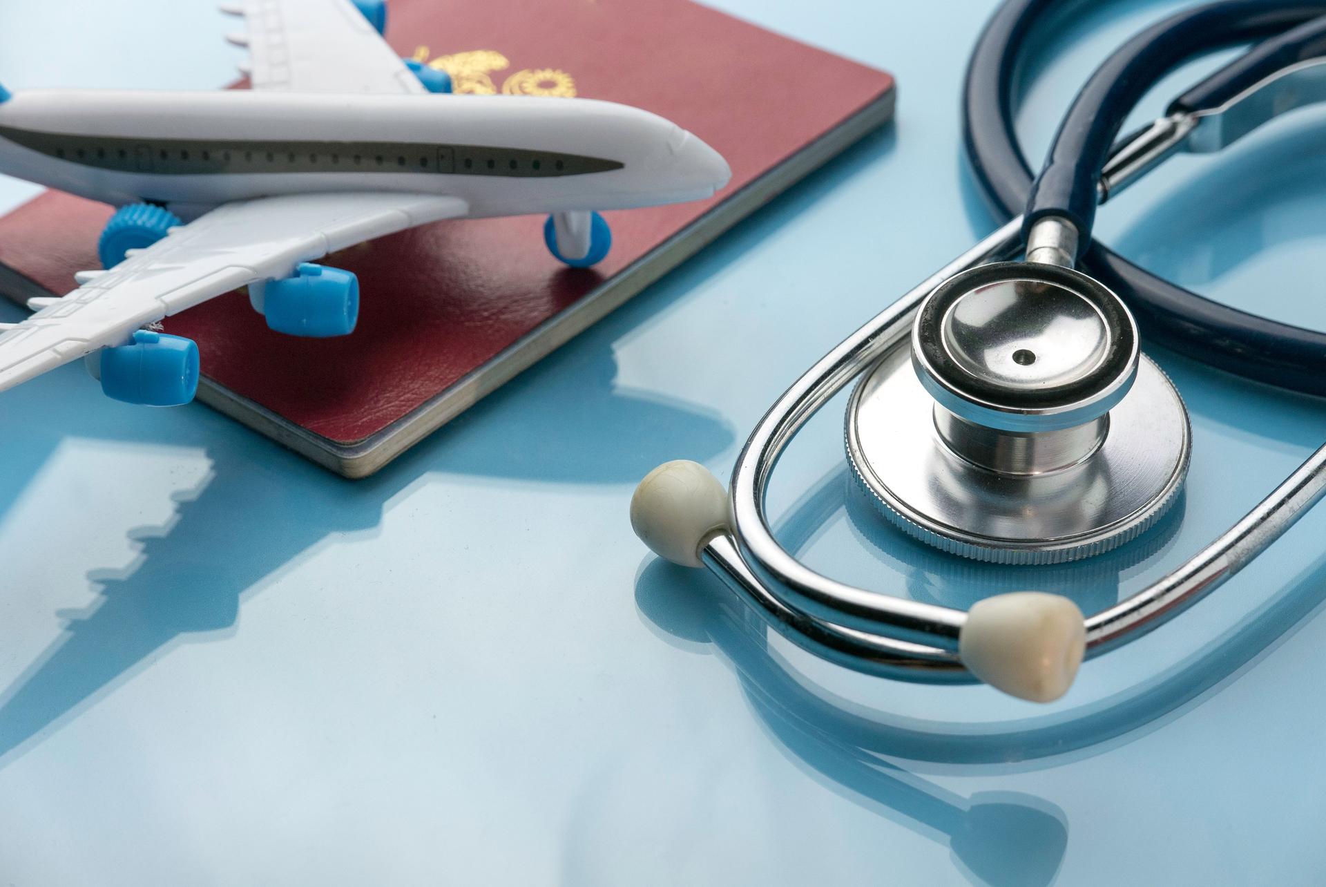 Healthcare,transportation and tourism concept with stethoscope, passport and plane model on a blue glass background.
